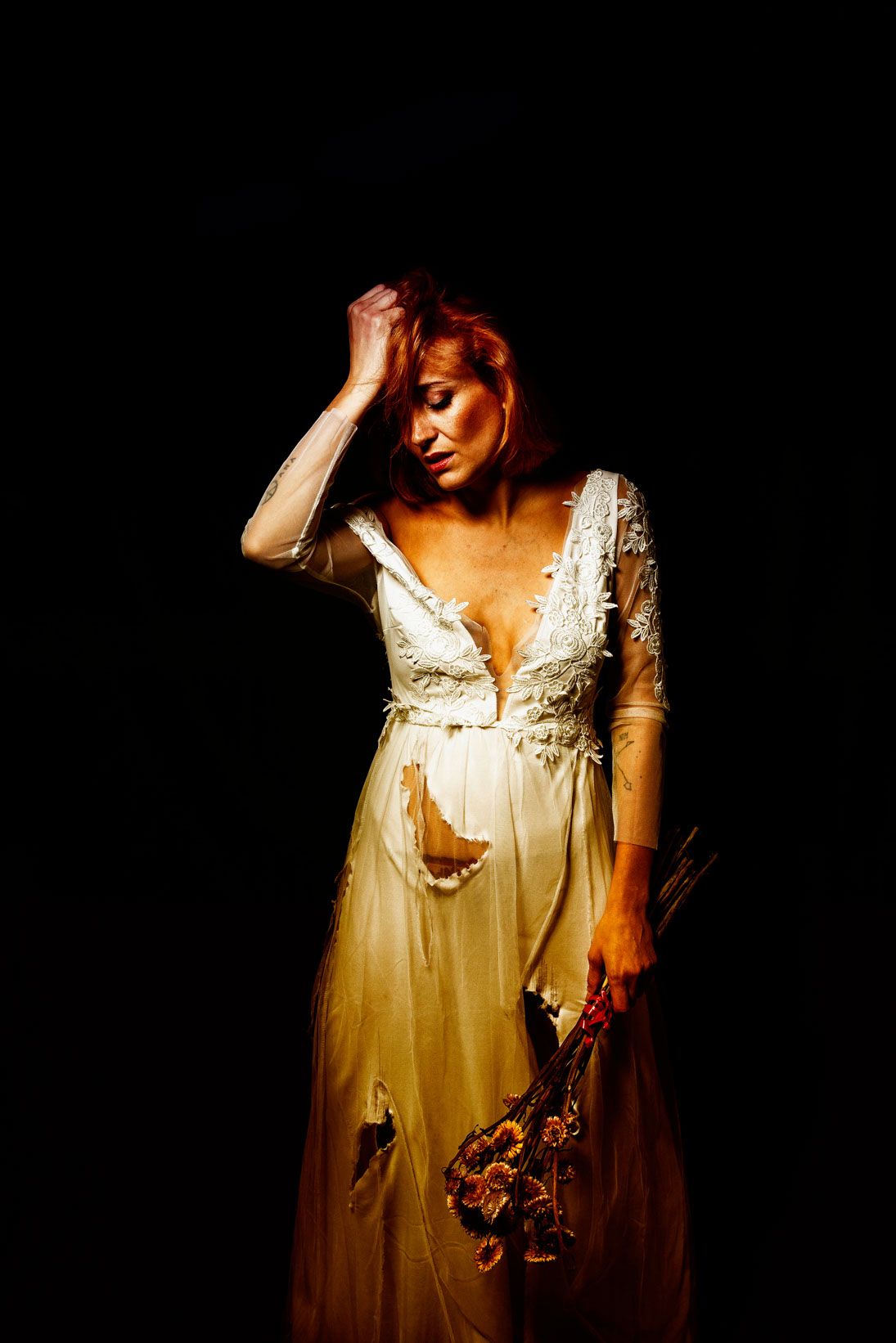 Woman in a white dress lit by a single warm light against a black background